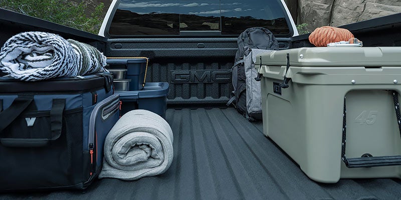 Camping gear in a GMC Canyon bed: coolers, blankets, backpack, and cooking pots