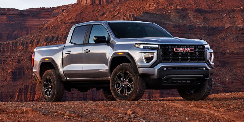2025 GMC Canyon parked on a rugged, reddish-brown terrain with a mountain backdrop.